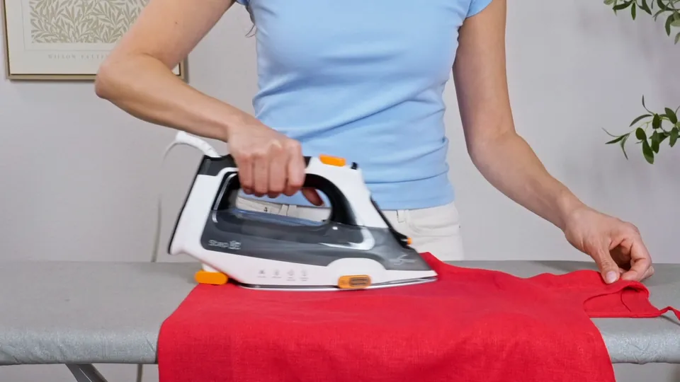 Steam iron gliding across a red shirt on an ironing board